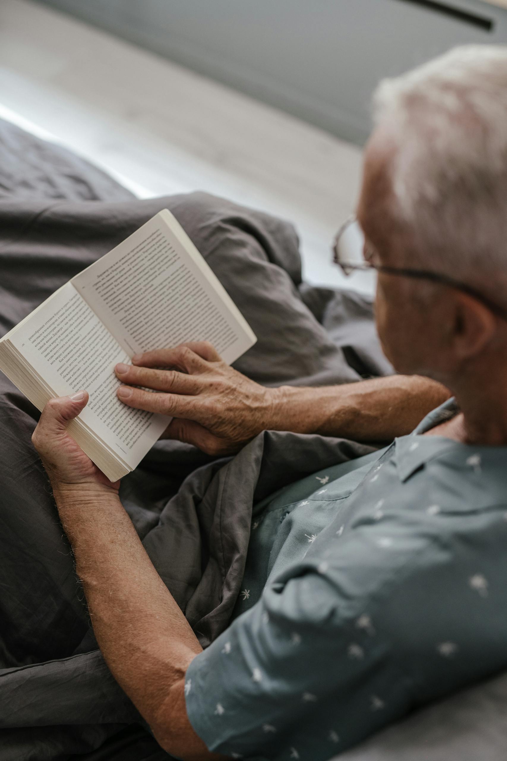 Elderly man reading a book in bed as part of hospital bag comfort and entertainment items